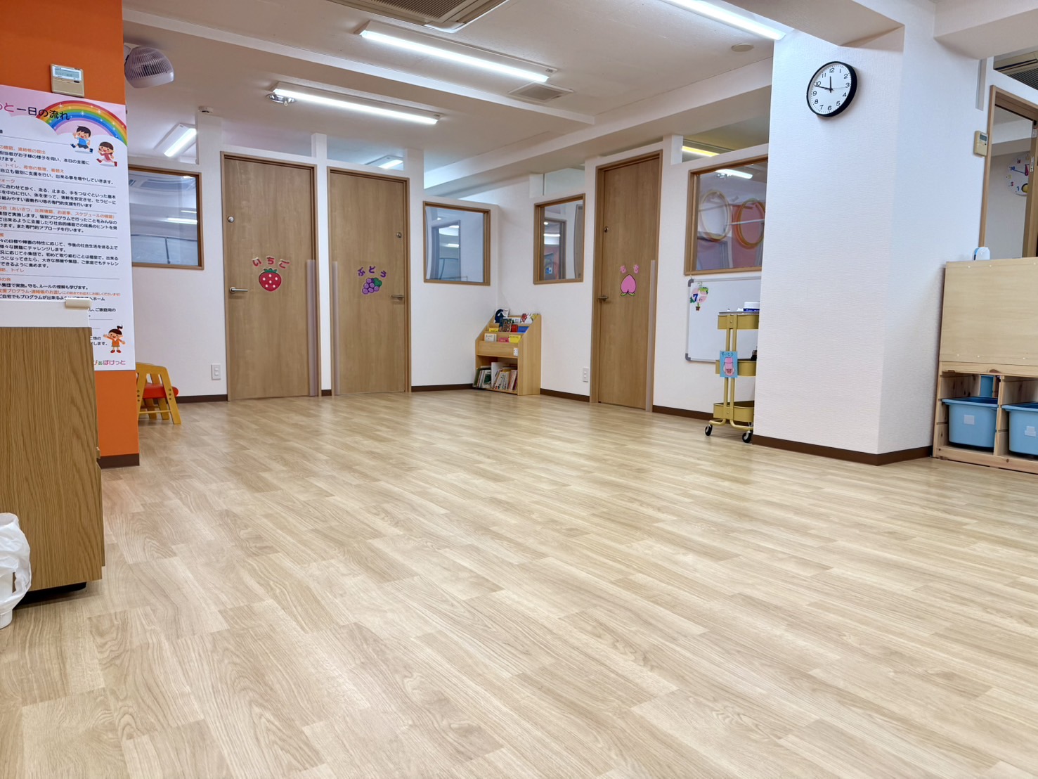 明るいフローリングの大部屋。奥に「いちご」「ぶどう」「もも」の個室の扉が並んでいる